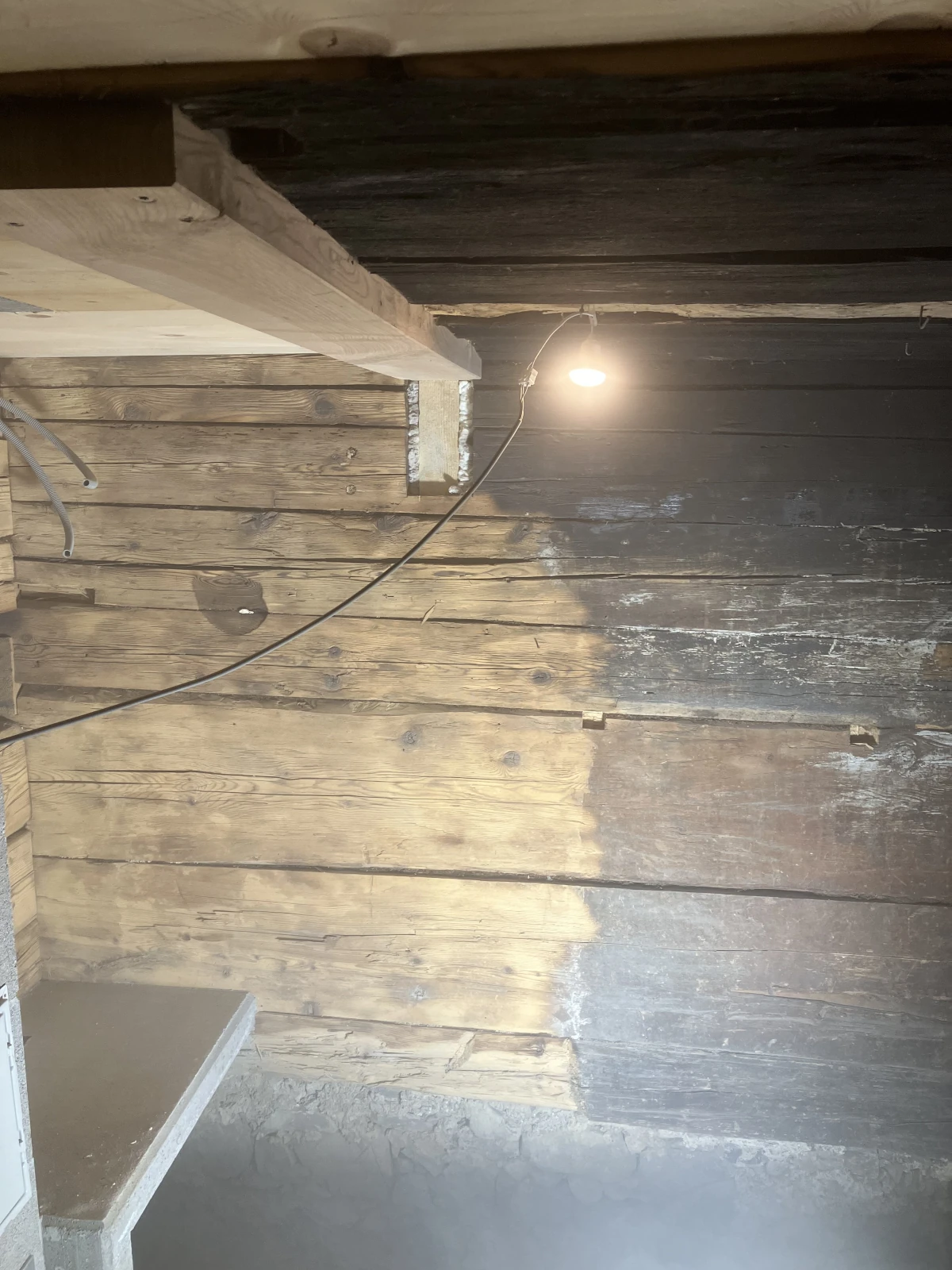 Eine rußgeschwärzte Holzwand neben einem Kamin die mit dem Sandstrahler zur Hälfte gereinigt wurde.