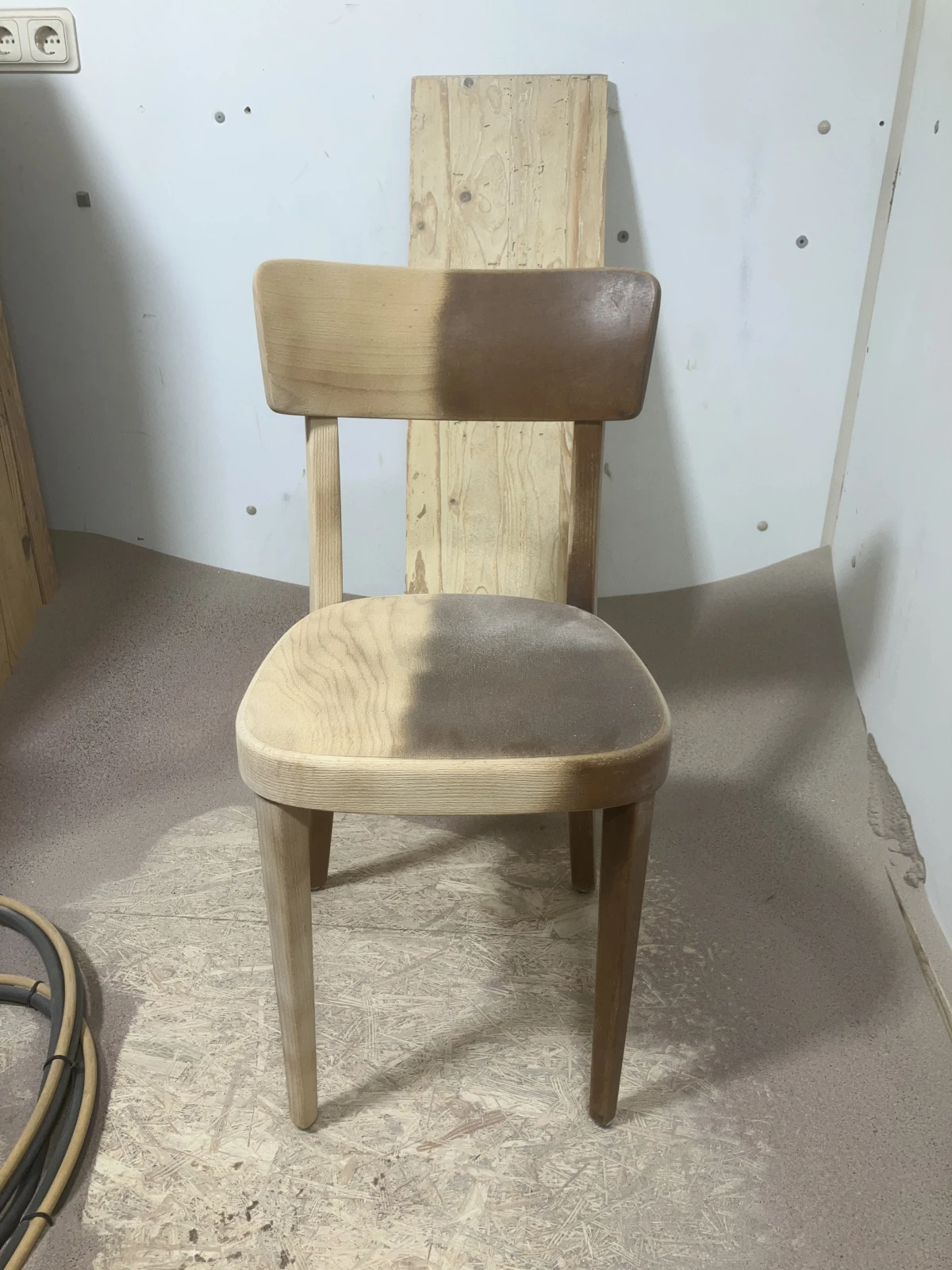 Ein Stuhl bei dem mit Sandstrahlen der Lack entfernt wird. Der halbe Stuhl ist fertig.